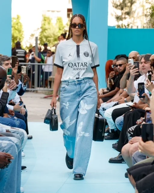Model on the 2023 runway wearing the grey PSG jersey and blue dove-print jeans.