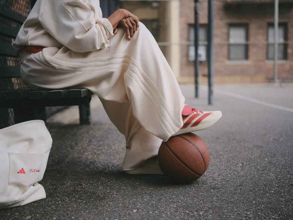 Detail of the cream tracksuit, red-striped shoes and branded tote beside a basketball.