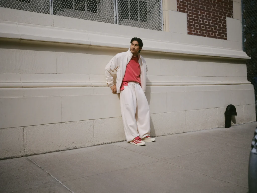 Model wearing a cream tracksuit over a red T-shirt against a courtside wall.