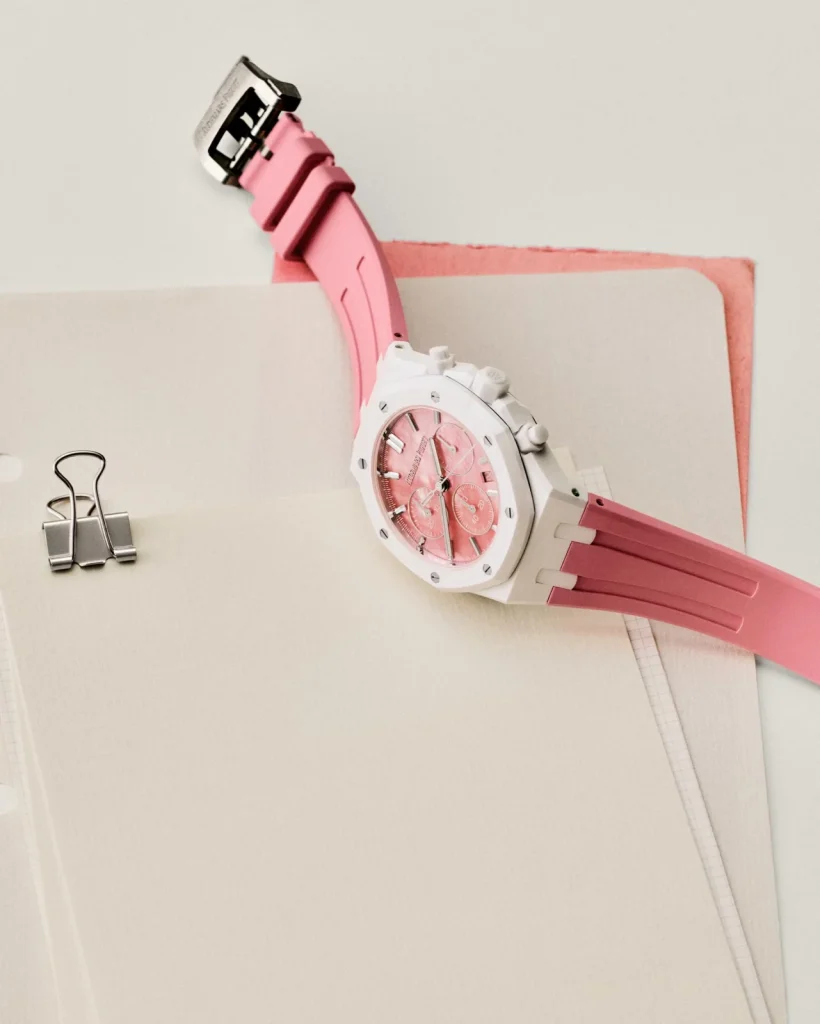 White ceramic Royal Oak with a pink rubber strap displayed on notebooks