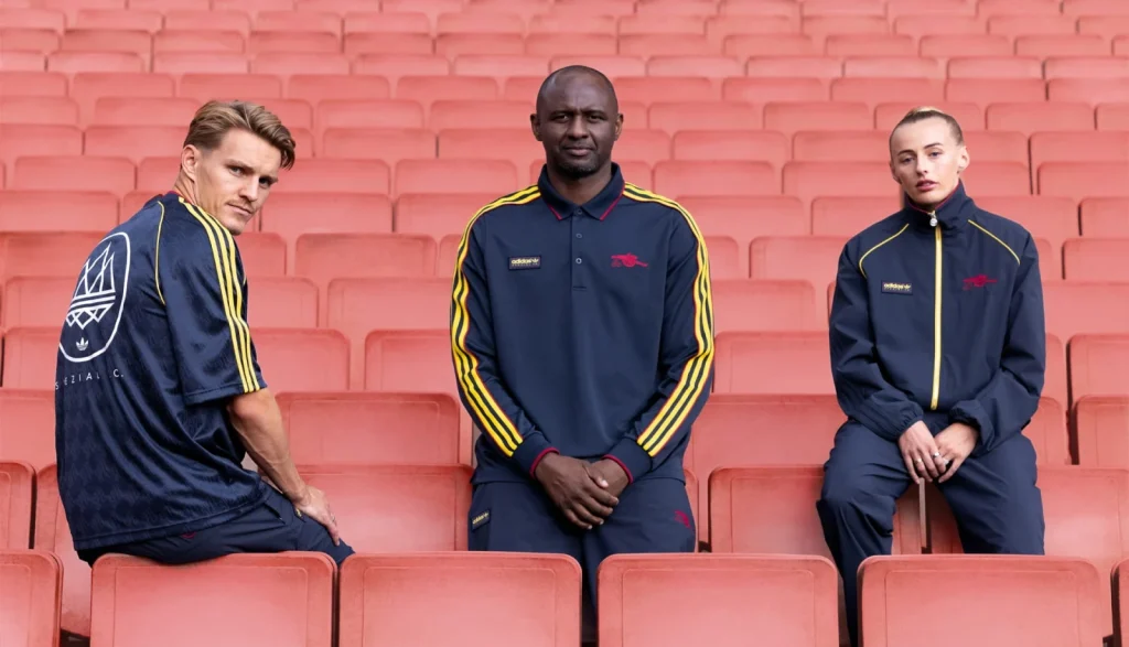 Martin Ødegaard, Patrick Vieira and Chloe Kelly in Arsenal adidas SPZL tracksuits on red stadium seats