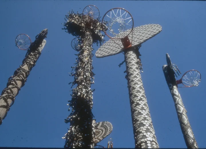 David Hammons’s Higher Goals: bottle-cap-covered poles topped with backboards and basketball hoops, photographed against the sky.