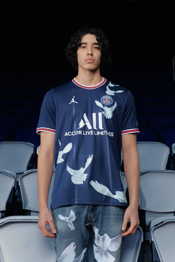Model wearing the blue PSG home jersey with large white doves in the 2022 collection.