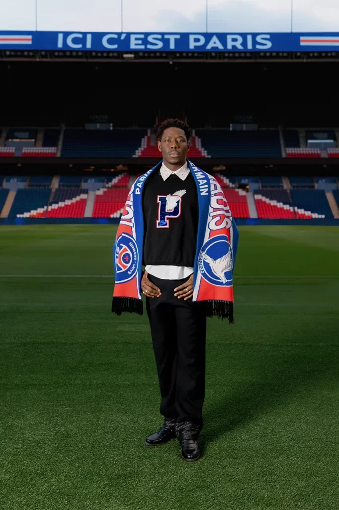Model wearing a red jacket, a large P motif and a scarf on the Parc des Princes pitch.