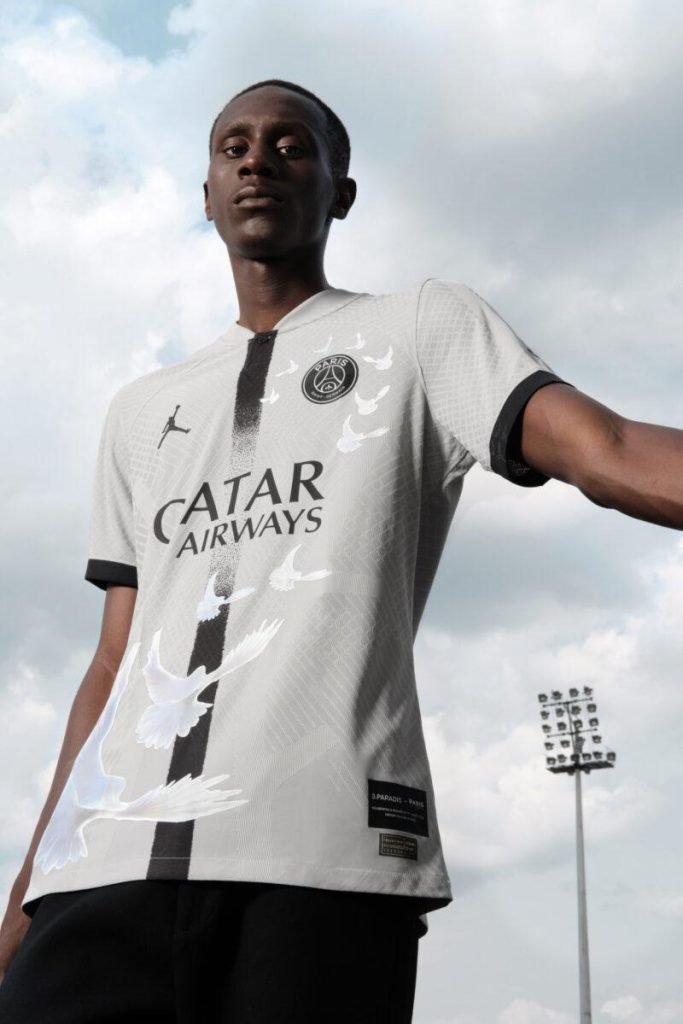 Model wearing the grey 2023 PSG and 3.PARADIS jersey with white doves and a black central stripe.