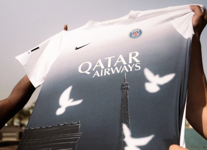 Hands hold the PSG × 3.PARADIS Art Basel Qatar pre-match shirt, with a white-to-blue gradient, white doves and Paris landmarks.